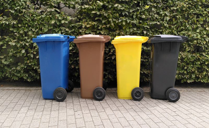 vier verschiedenfarbige Mülltonnen, die nebeneinander vor einer Hecke stehen