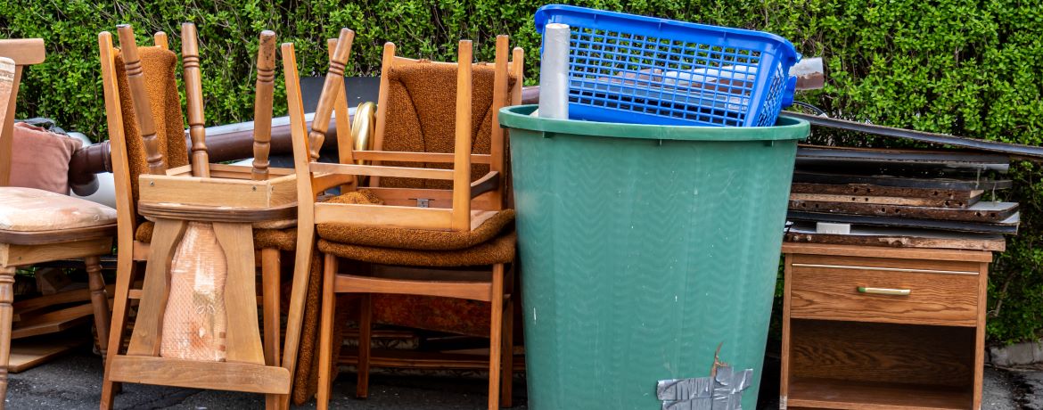 Sperrmüll (Möbel, Kunststofftonne, Kinderspielküche) steht vor einer Hecke